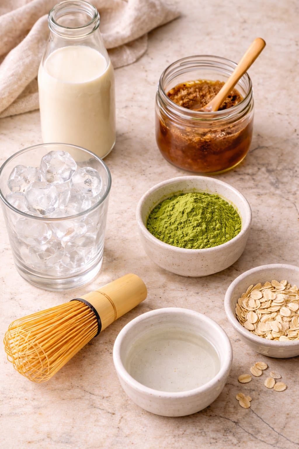 Ingredients for iced matcha brown sugar oat milk latte including matcha powder, brown sugar syrup, oat milk, ice, and water
